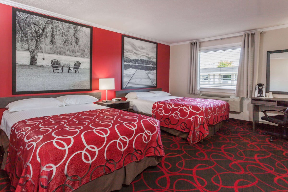 A hotel room with two beds, a desk, a chair, a lamp, and two large framed pictures on the wall.