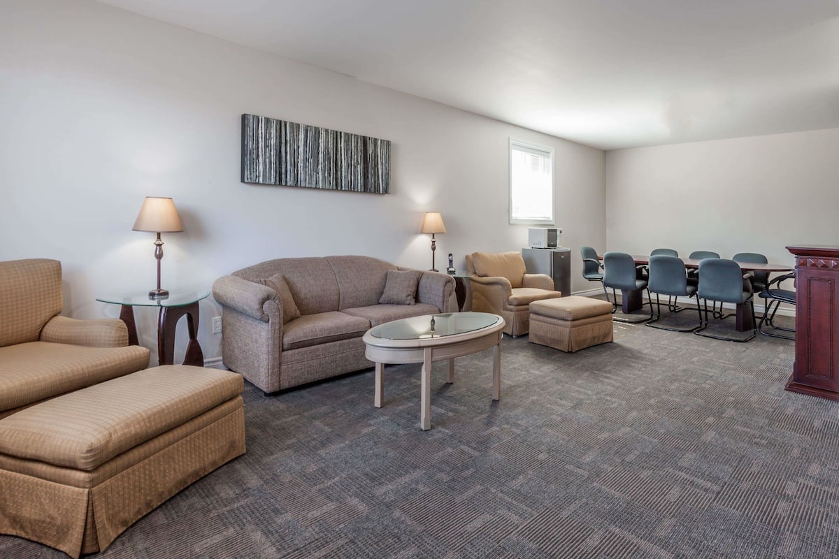 A hotel room with a sofa, armchairs, a small table, a desk, and a conference table with chairs.