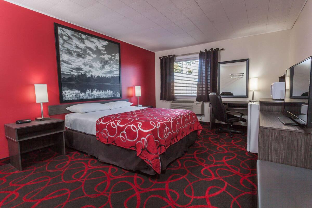 A hotel room with a bed, desk, chair, and a large window with curtains.