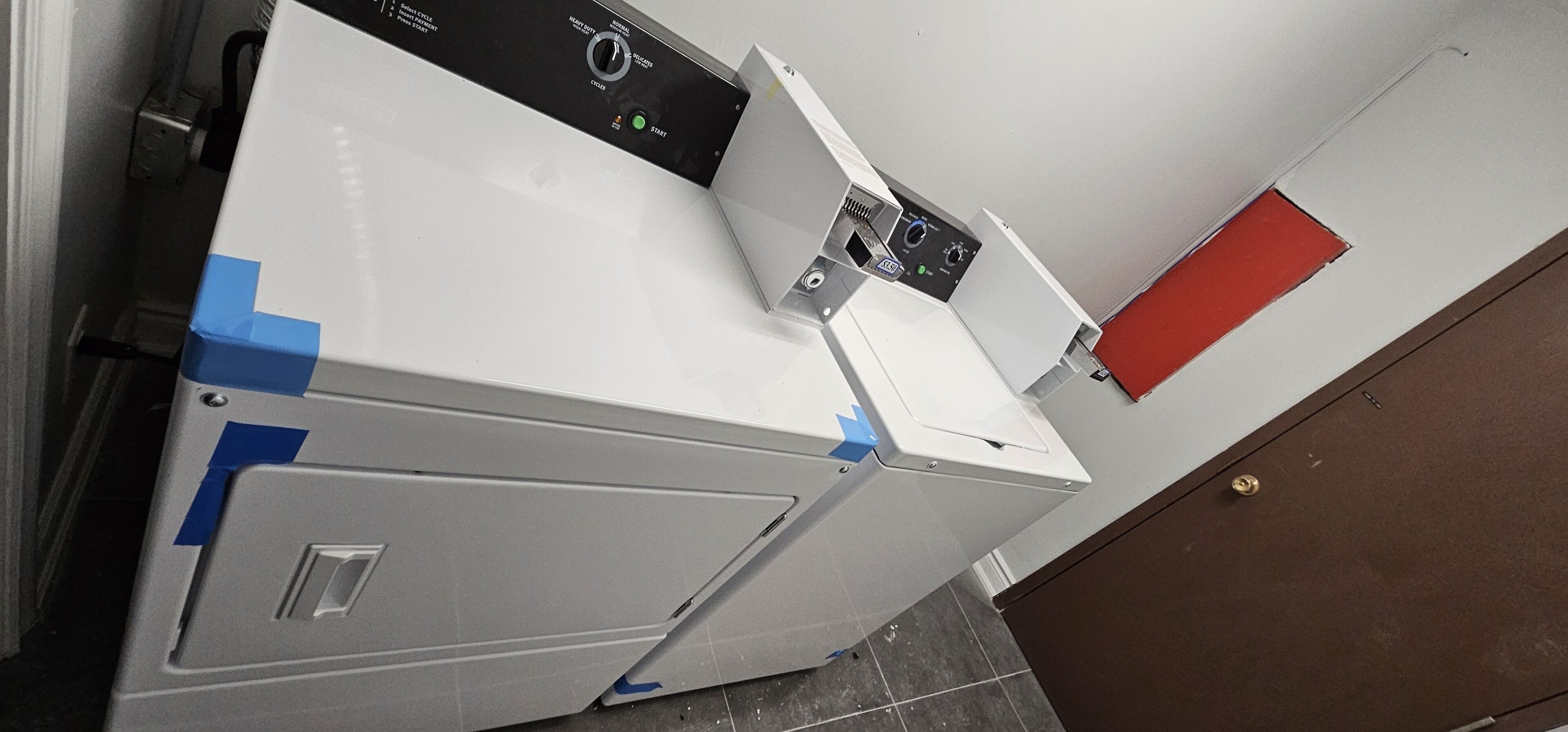 A white washing machine with a control panel, blue tape on the side, and a red door in the background.