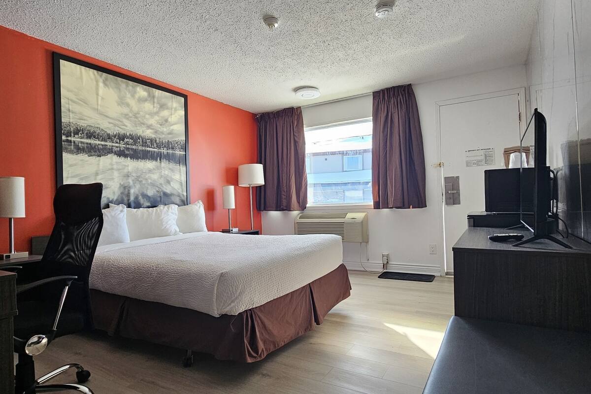 A hotel room with a large bed, a desk, a chair, a TV, and a window with curtains.