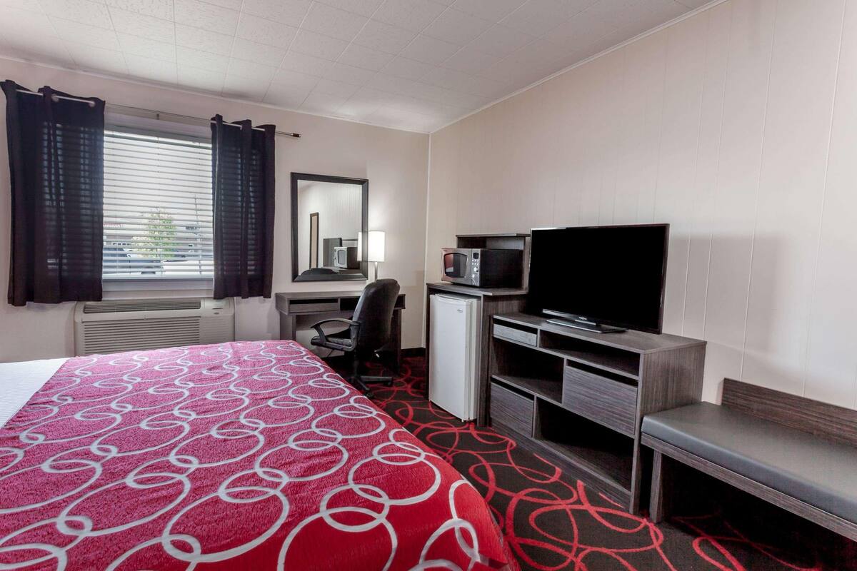 A hotel room with a bed, a desk with a computer, a television, a microwave, and a small refrigerator.