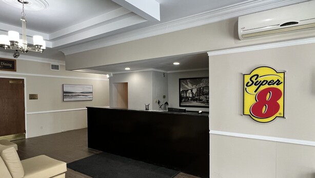 A reception area with a black reception desk, a beige sofa, a black rug, a painting on the wall, and a 'Super 8' sign. - Super 8 by Wyndham Kirkland Lake (Kirkland Lake)