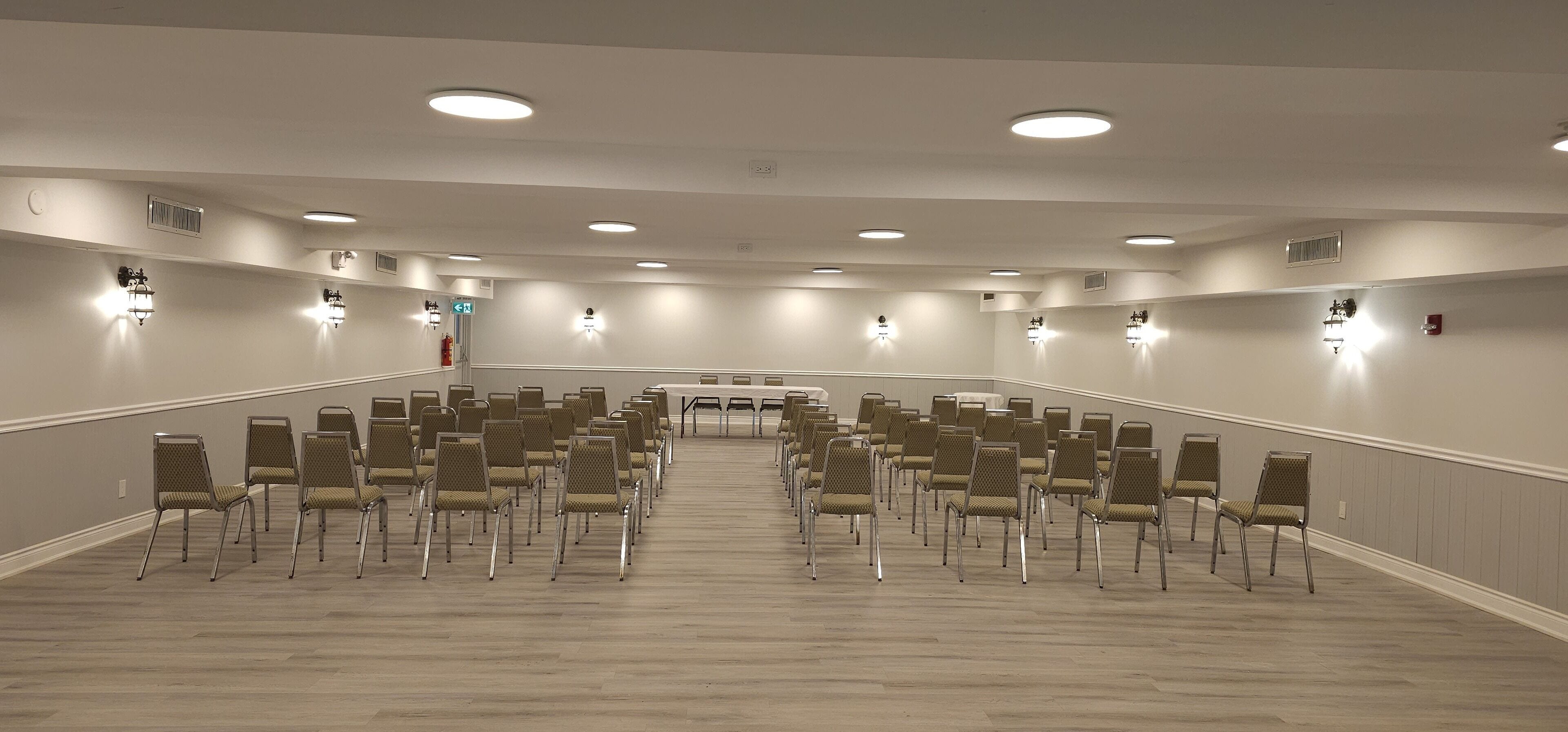 Konferenssihuone, jossa on riveissä tuoleja, keskellä suuri pöytä ja upotetut valaisimet.