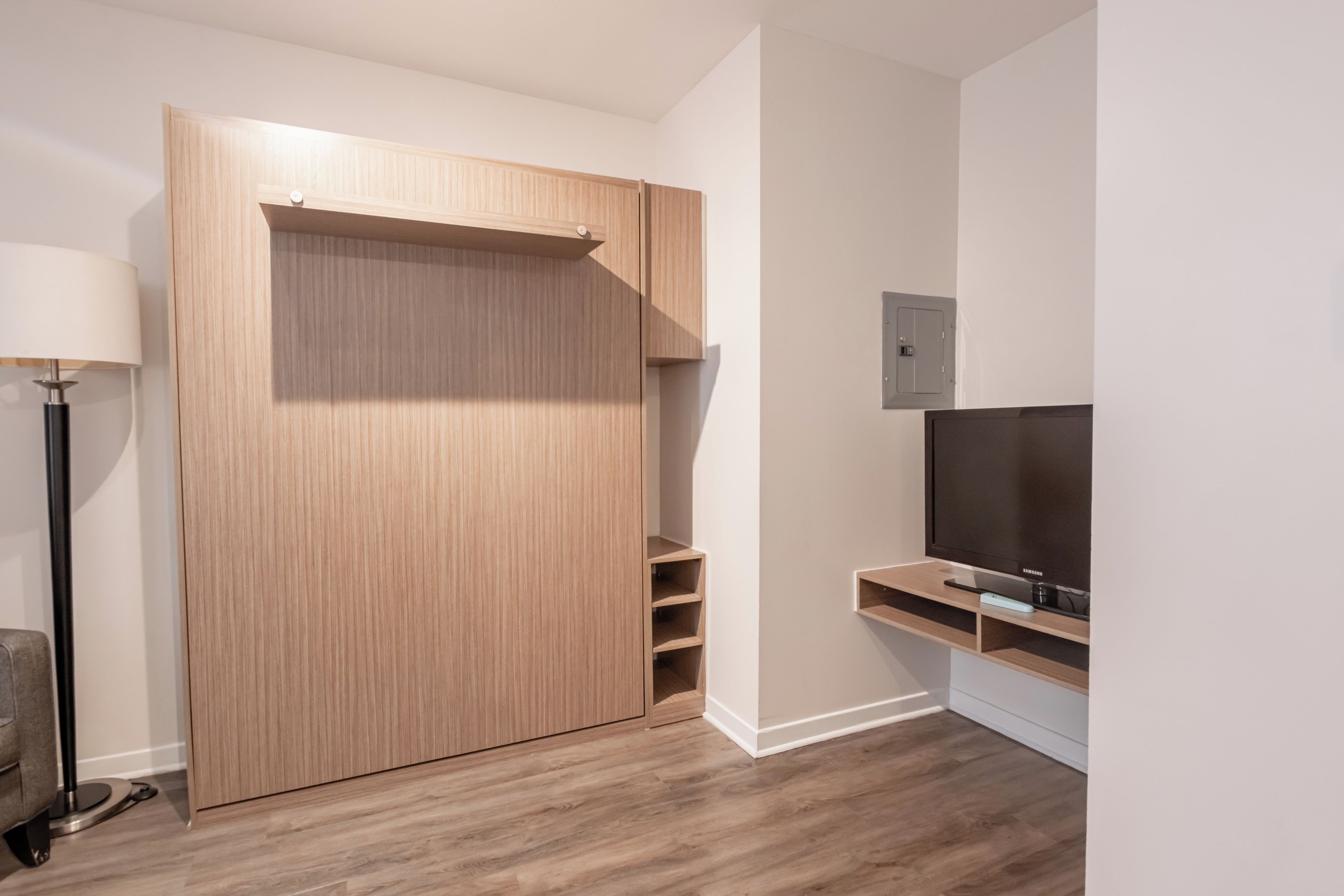 Une pièce avec une armoire en bois, un téléviseur posé sur un meuble en bois et un lampadaire.