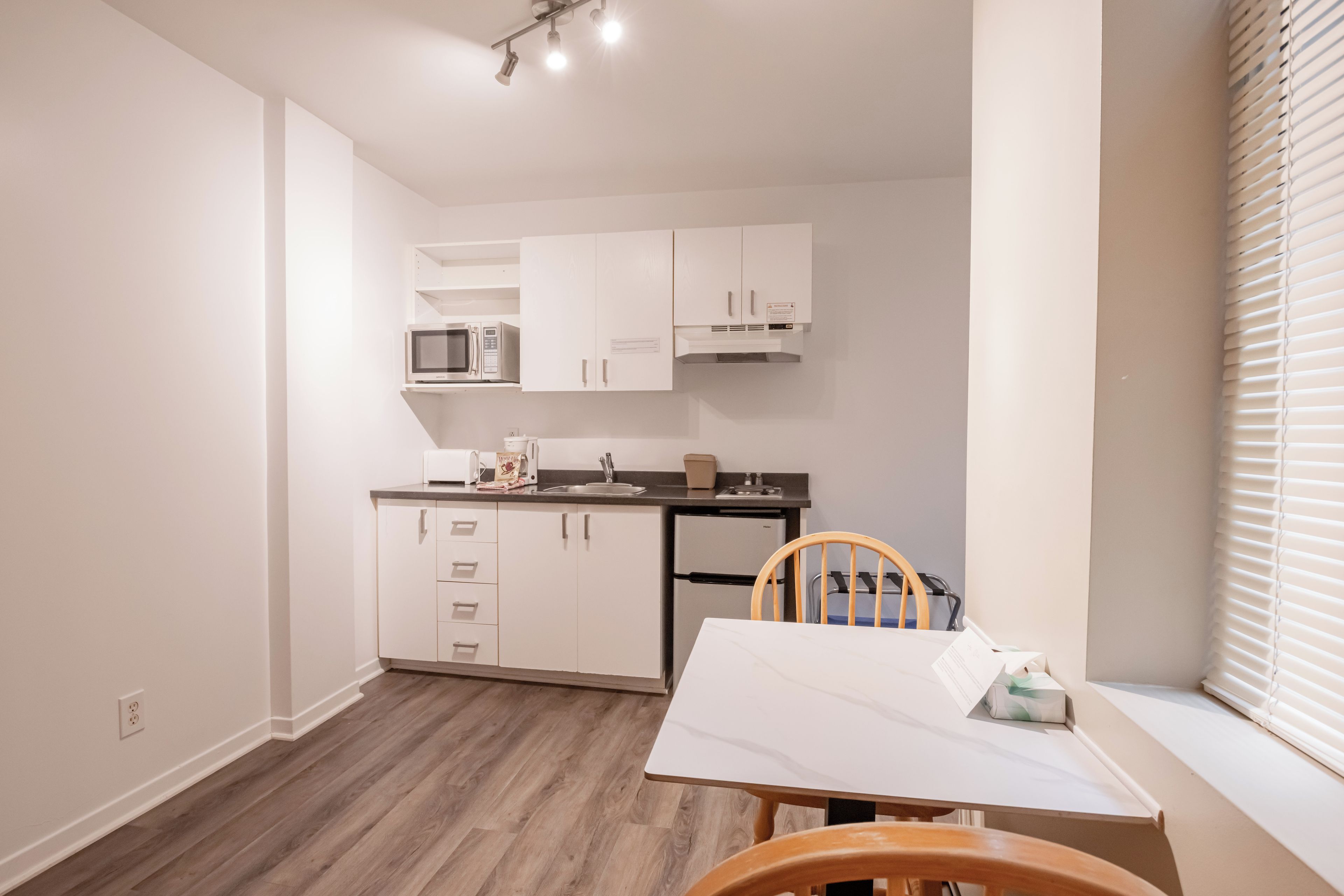 A compact kitchen with white cabinets, a microwave, a refrigerator, and a dining table with a chair.