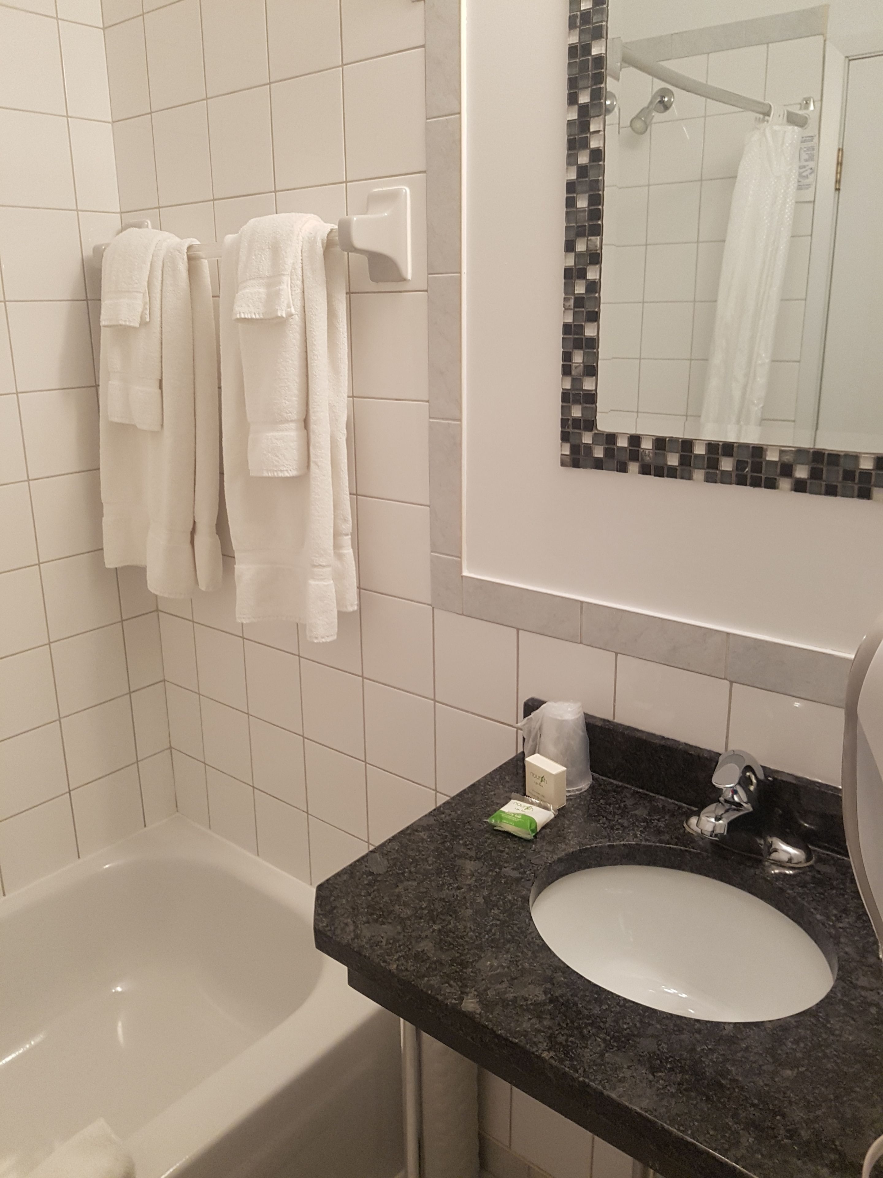 Une salle de bain avec une baignoire blanche, un lavabo doté d’un plan-vasque noir et un miroir orné d’une bordure en mosaïque.