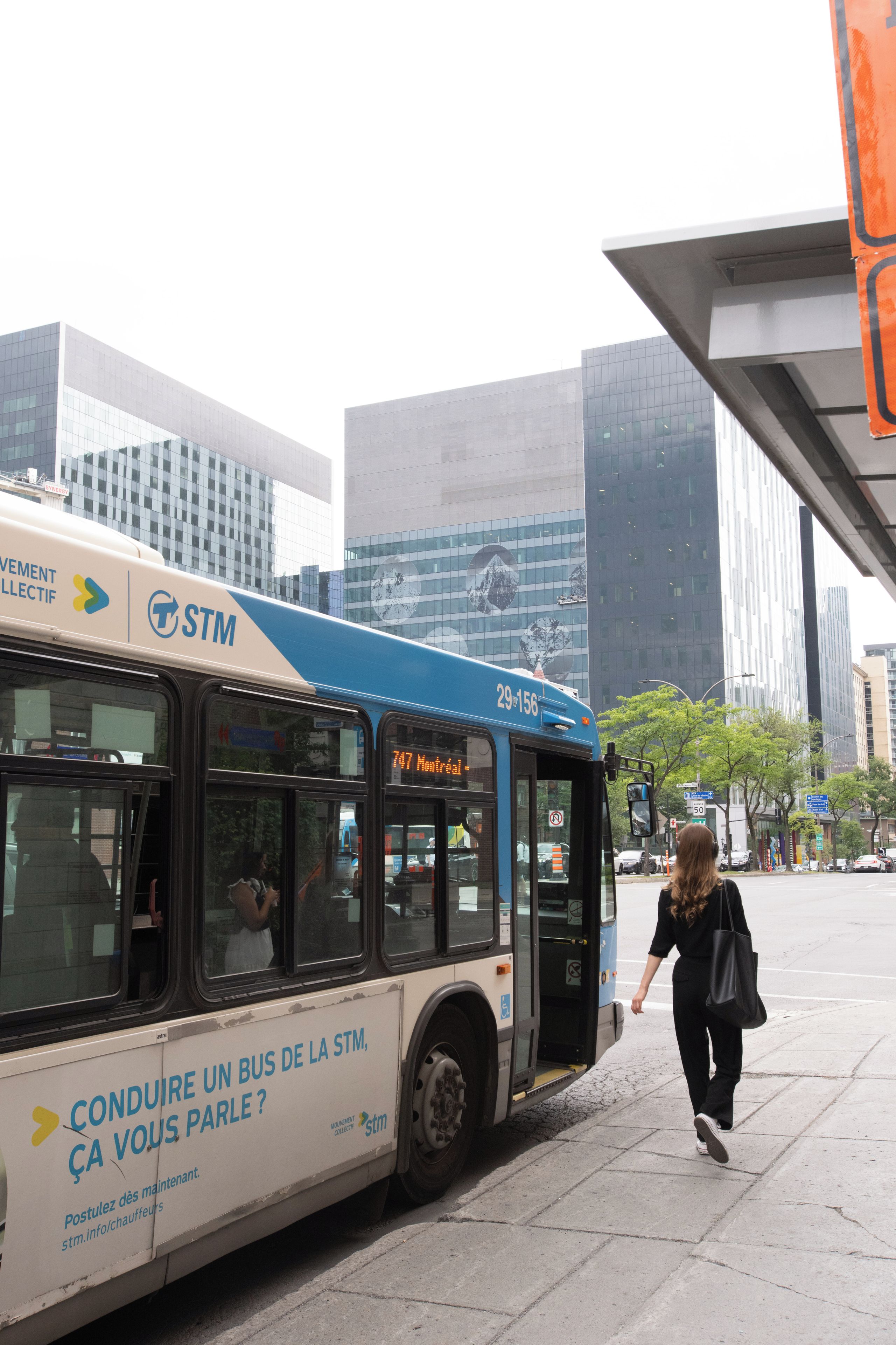 A bus with 'STM' and 'Conduire un bus de la STM' text, parked on a city street with modern buildings in the background.