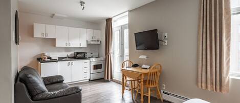 A modern room with a sofa, a dining table with chairs, a TV mounted on the wall, and a kitchen area with cabinets and appliances.