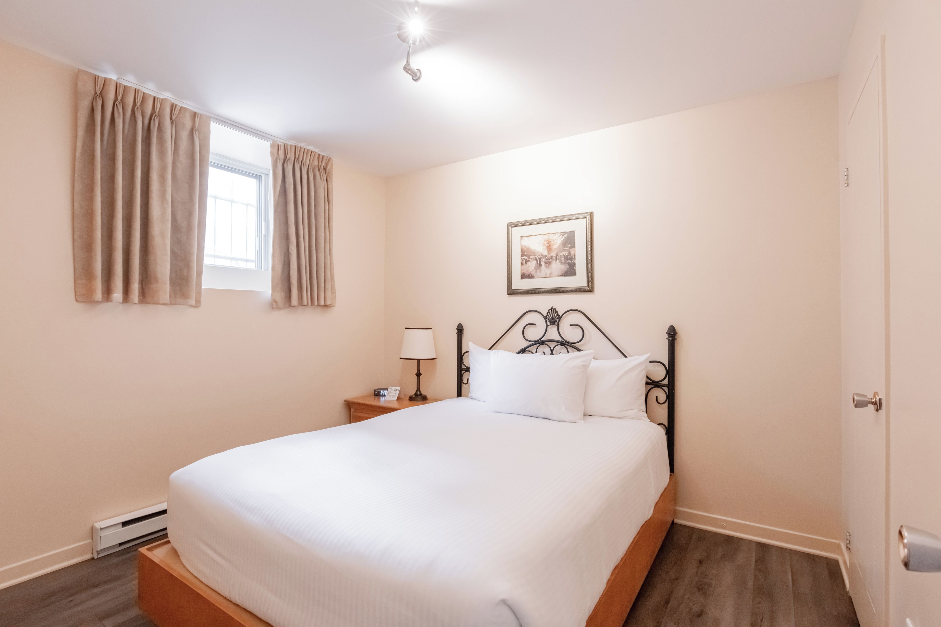 A hotel room with a bed, a nightstand, a lamp, a framed picture on the wall, and a window with curtains.