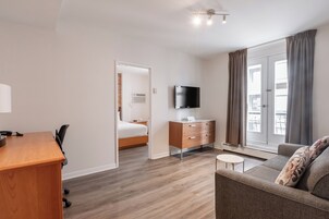 A hotel room with a wooden desk, a bed, a TV, a sofa, and a window with curtains.