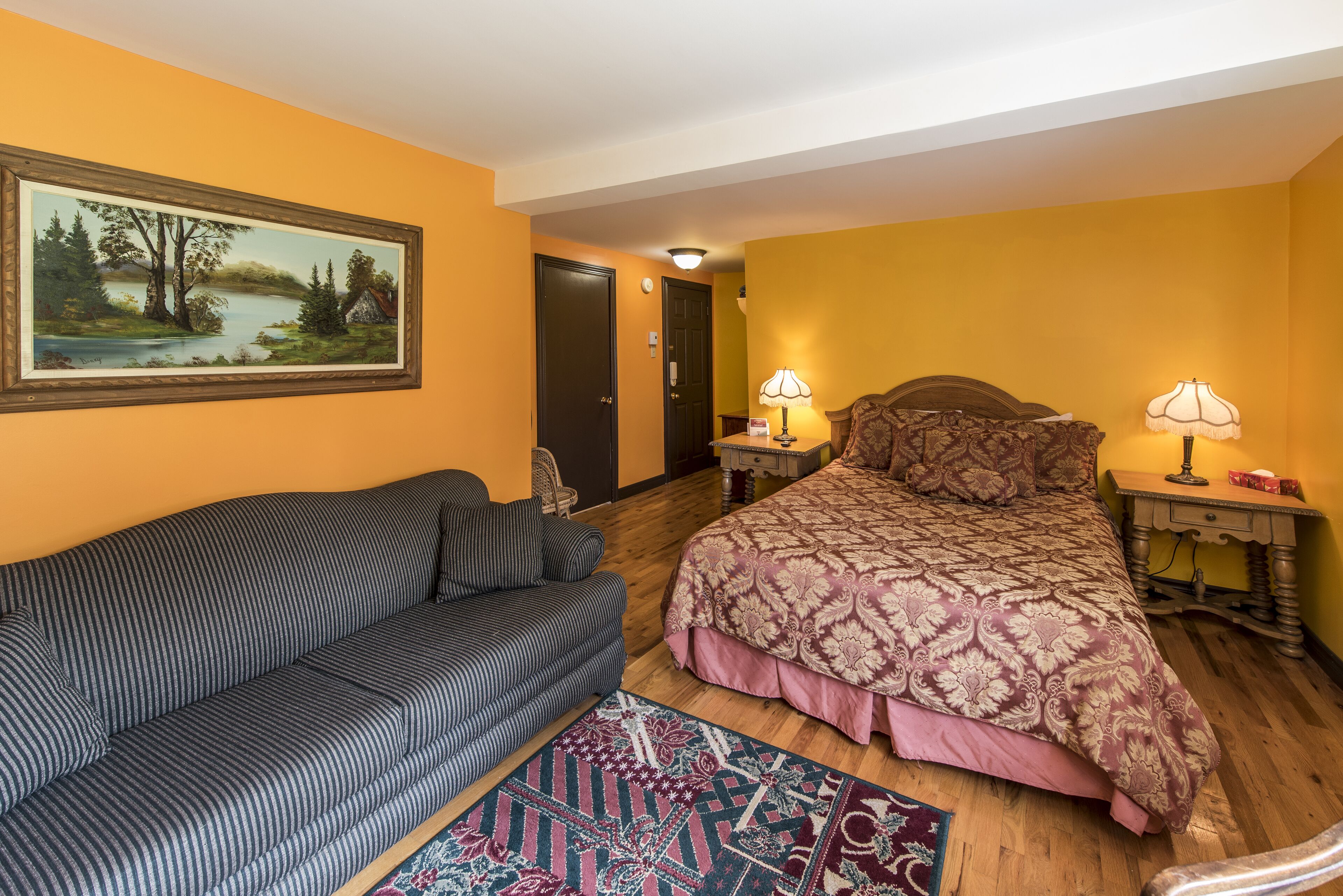 A bedroom with a bed, a sofa, a painting, and a rug.