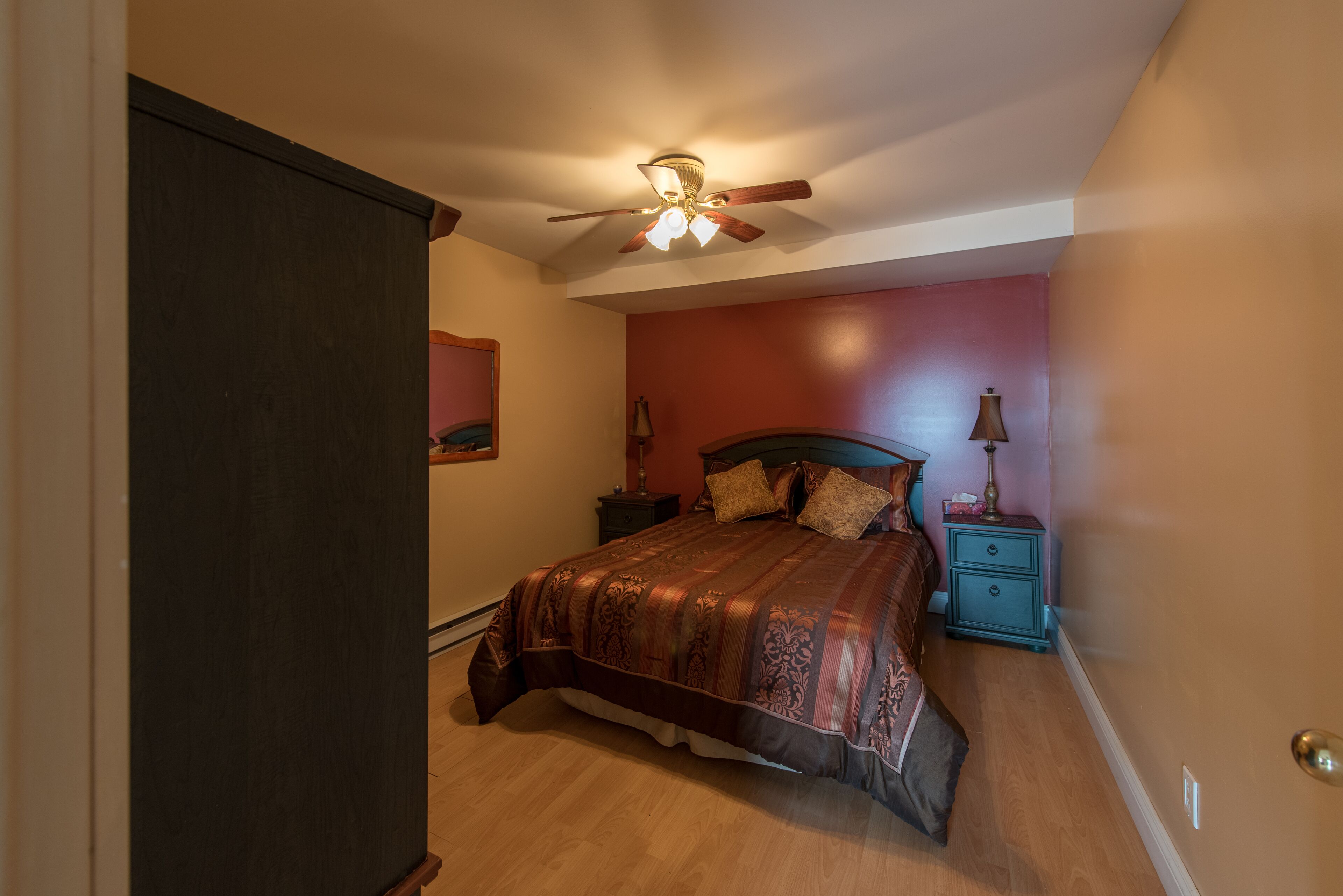 A bedroom with a bed, nightstand, lamp, and ceiling fan.