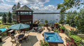 A deck with a hot tub, lounge chairs, and a gazebo overlooking a lake.