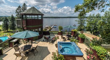 Une terrasse dotée d’un jacuzzi, de chaises longues et d’un belvédère offrant une vue sur un lac.
