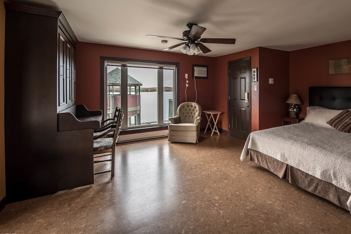 Ein Schlafzimmer mit einem großen Bett, einem Sessel, einem Deckenventilator und Blick auf ein Gebäude durch das Fenster.