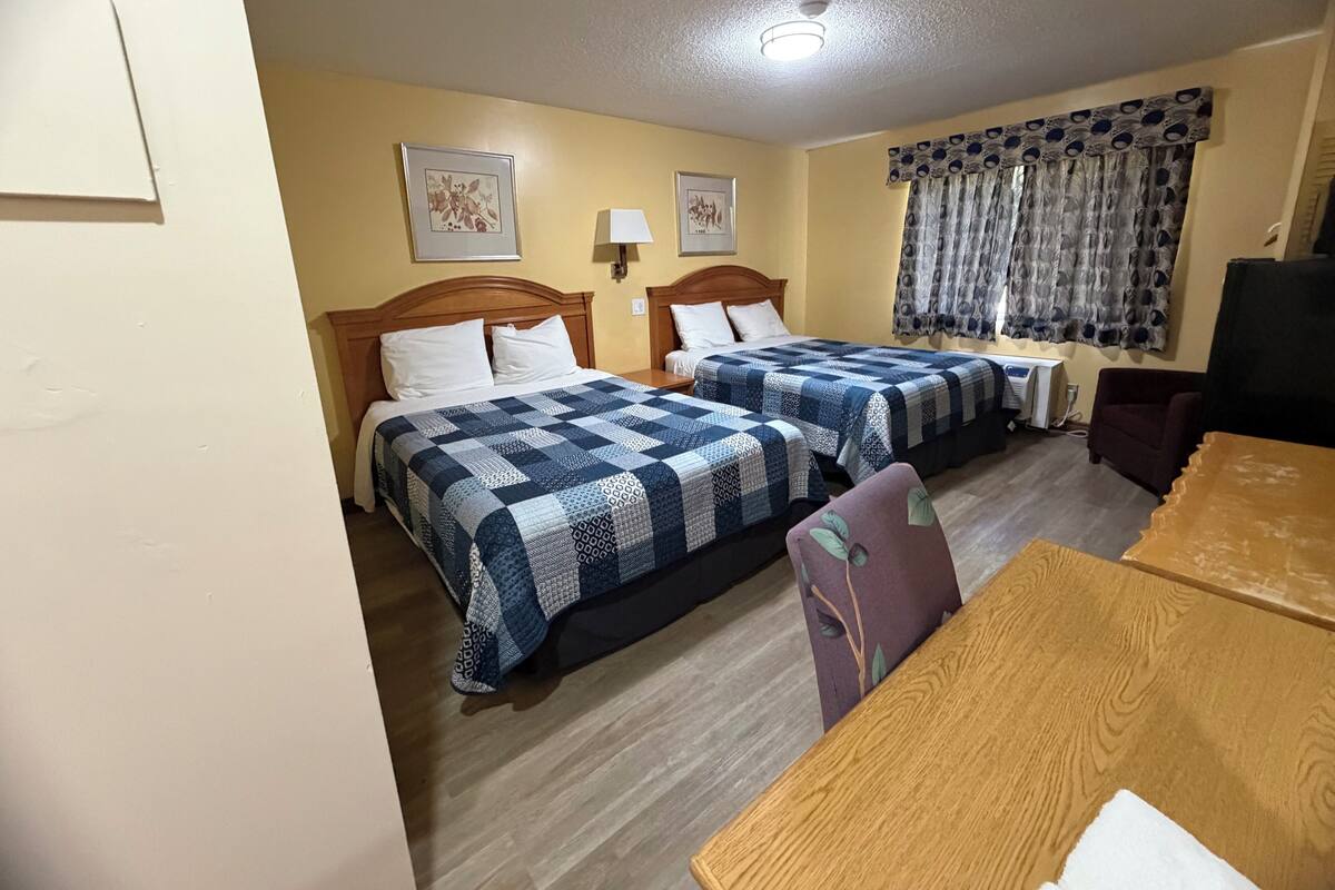 A hotel room with two beds, a wooden table, a chair, a television, and a window with patterned curtains.