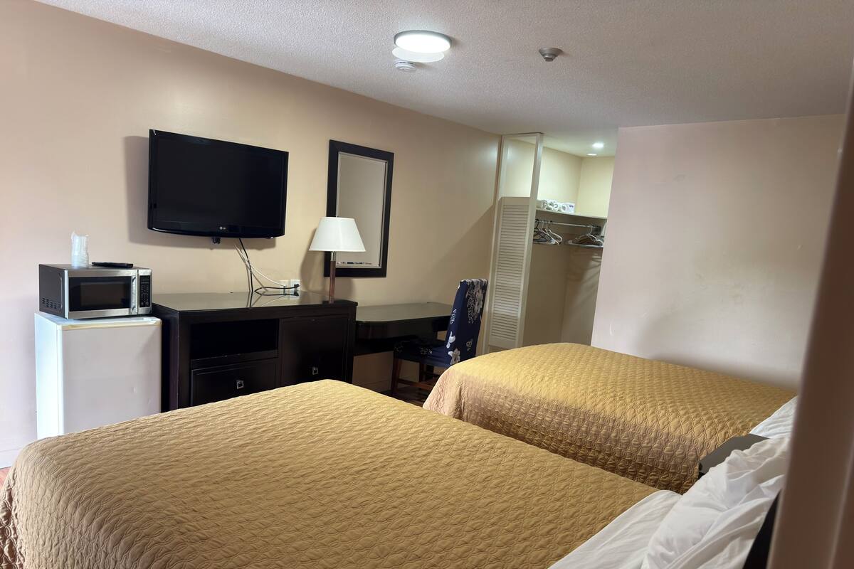 A hotel room with two beds, a desk with a computer, a TV, a lamp, and a wardrobe.
