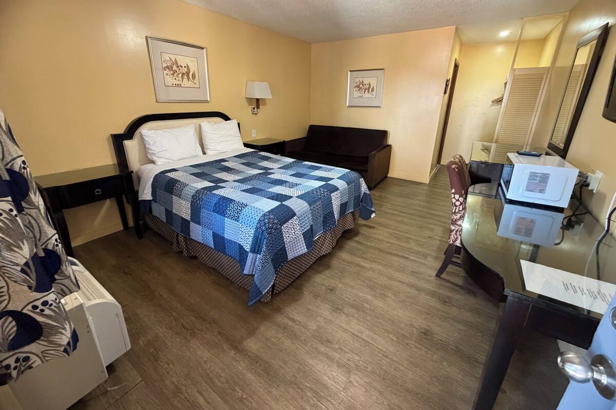 A hotel room with a bed, bedside table, lamp, dresser, mirror, and a small table with a microwave.