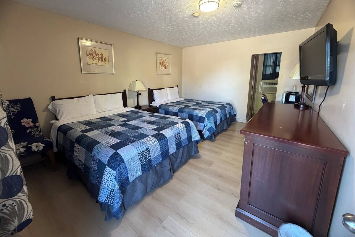 A hotel room with two beds, a wooden desk, a television, and framed artwork on the walls.