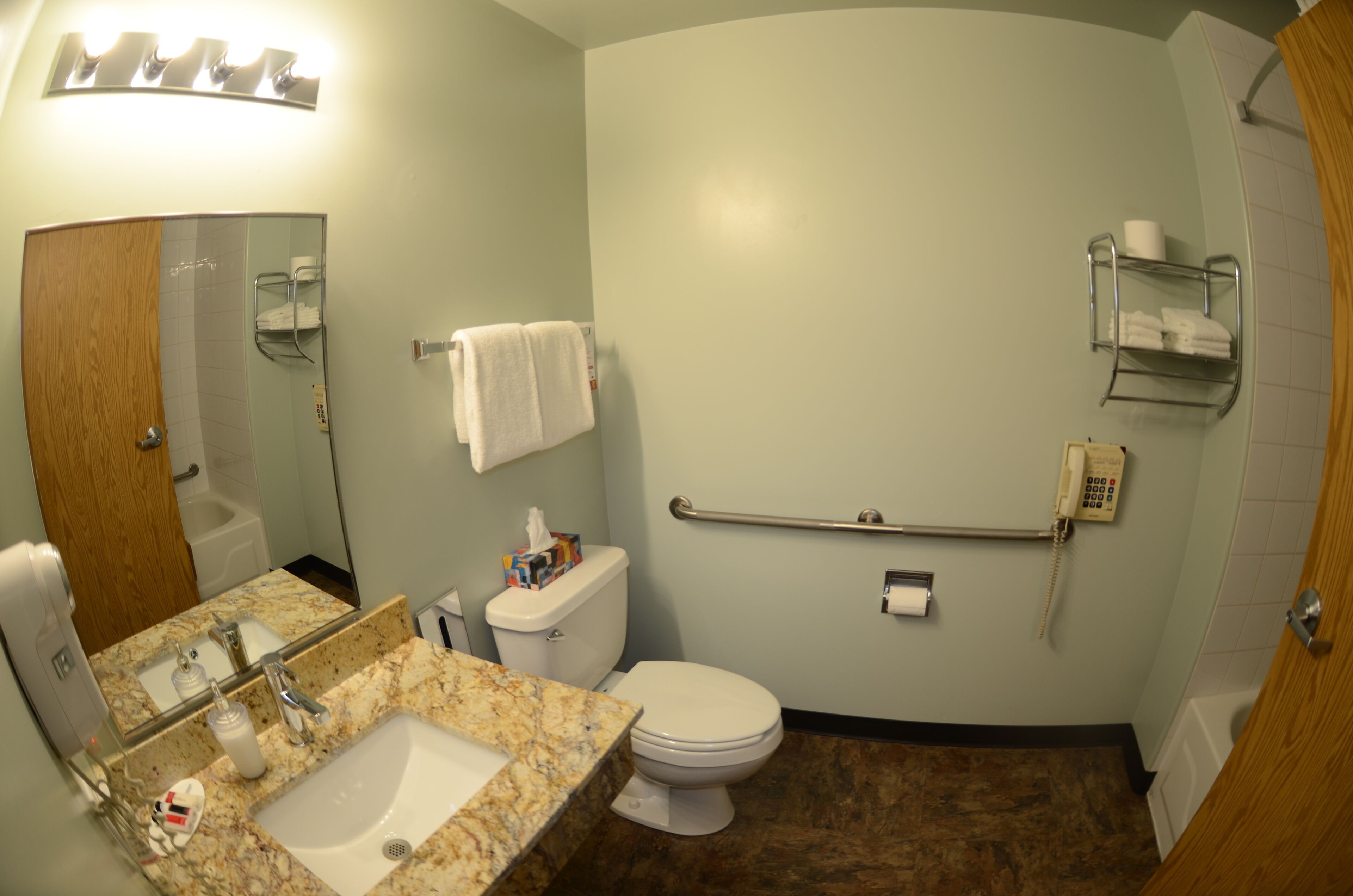 Une salle de bain équipée d’un lavabo en marbre, de toilettes et d’une barre d’appui pour faciliter l’accès aux personnes à mobilité réduite.