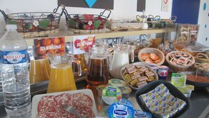 Un bufé con diversas opciones de comida y bebidas, incluyendo una botella de agua Cristaline, un plato de salami y varios recipientes de yogur.