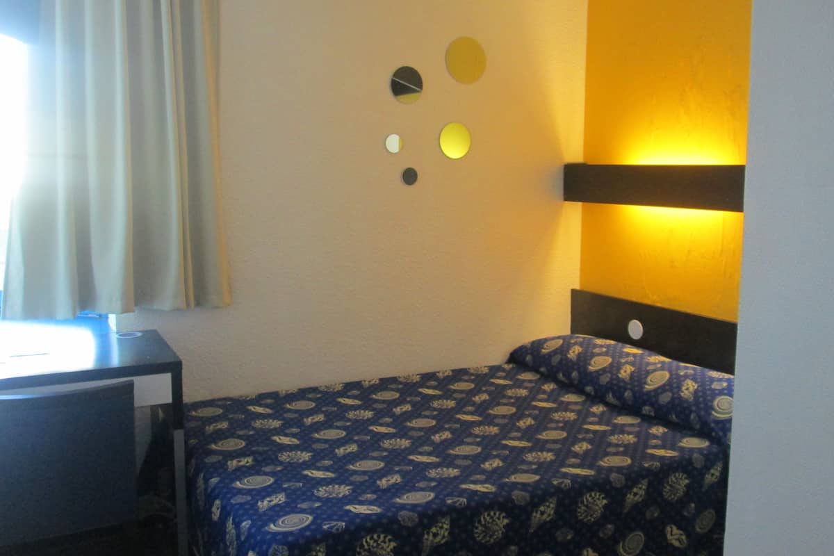 Een hotelkamer met een bed, een bureau, een raam met gordijnen en ronde decoraties aan de muur.