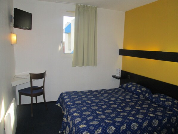 A hotel room with a bed, a desk, a chair, a television mounted on the wall, and a window with curtains. - Hotel Stars Dijon Sud (Chenove)