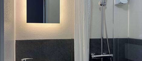 Un baño moderno con ducha, lavamanos y espejo.