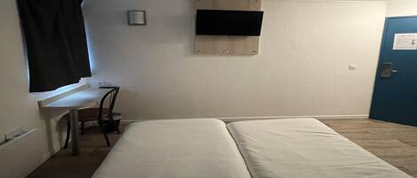 A room with a bed, a desk, a chair, a TV mounted on the wall, and a door.