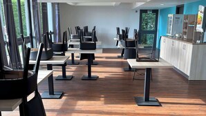 A spacious room with multiple tables and chairs, large windows, and a wooden floor. - Kyriad Direct Dreux (Dreux)