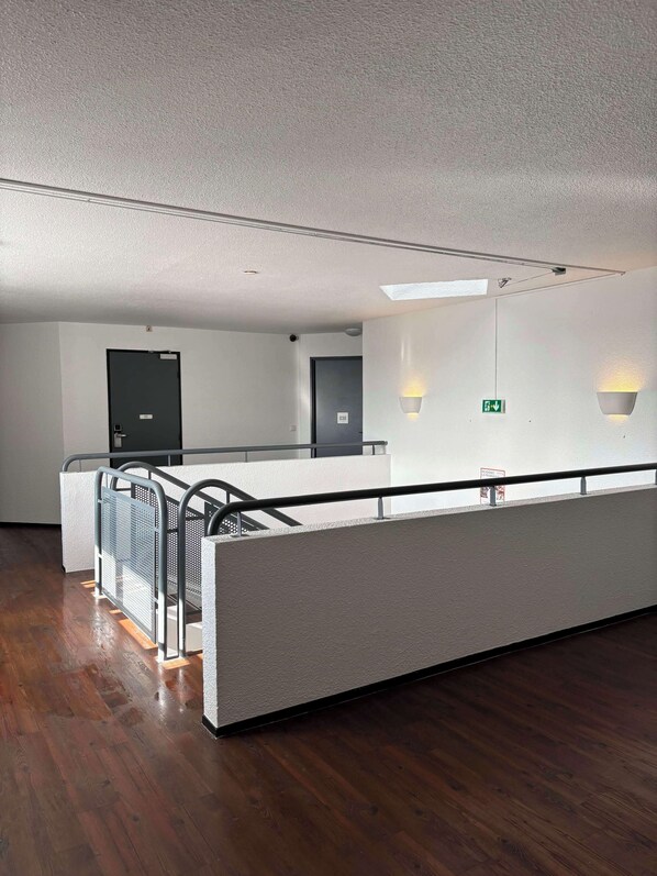A modern hotel lobby with a long reception desk, a staircase, and a wooden floor.