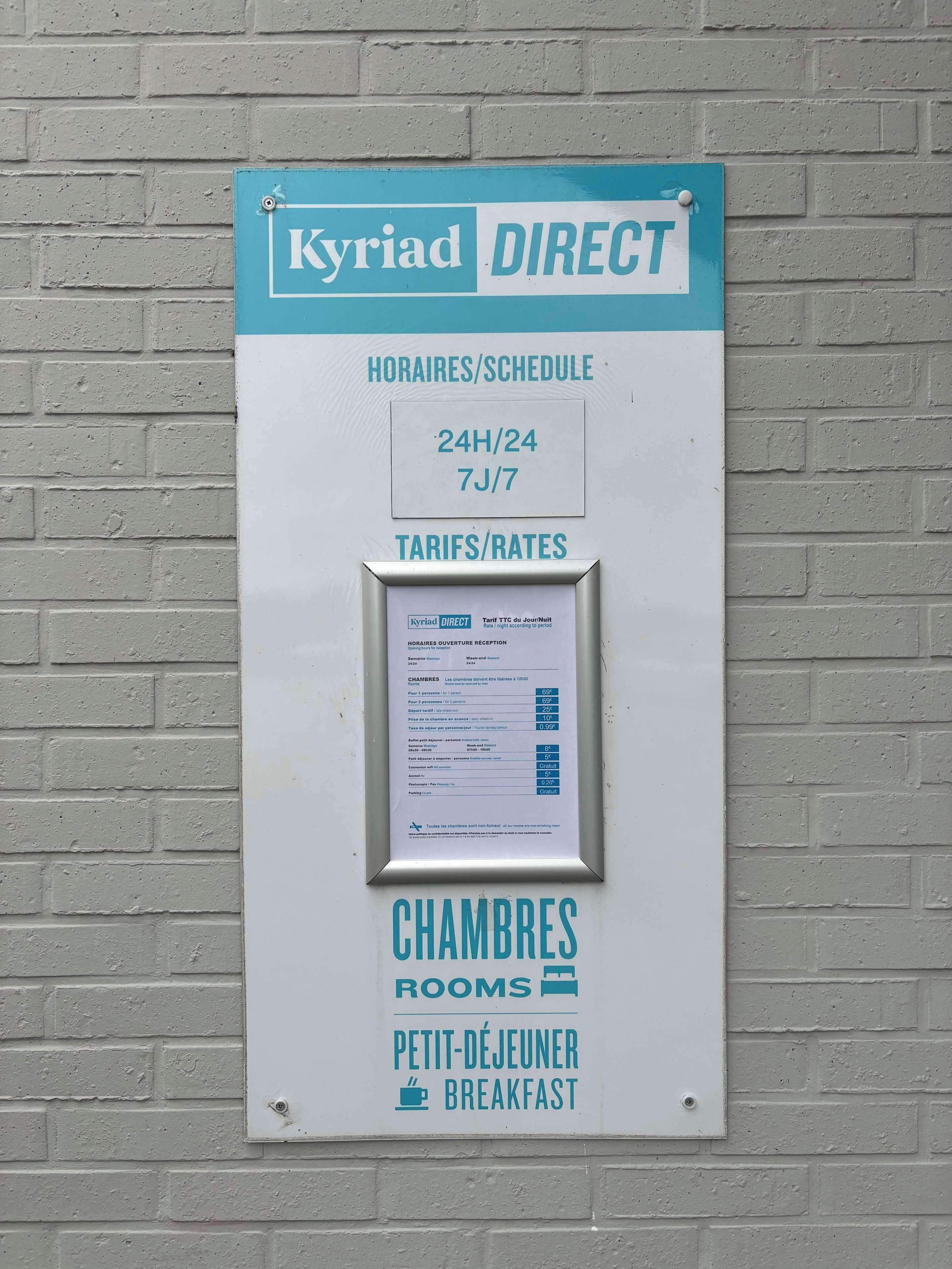 A signboard for Kyriad Direct hotel with 24/7 availability, room rates, and amenities like rooms, breakfast, and a small café.