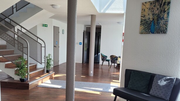 A spacious lobby with a wooden floor, a staircase with metal railings, a bench, and a peacock painting on the wall. - Kyriad Direct Dreux (Dreux)