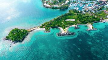 An aerial view of a tropical island with clear turquoise waters, a small beach, and a marina with boats.
