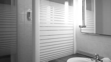 A modern bathroom with a glass shower enclosure, a white sink with a dark countertop, and a mirror with a chrome frame.