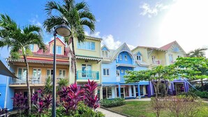 A row of colorful houses with balconies, surrounded by tropical plants and a clear sky. - Village Creole (Trois-Ilets)