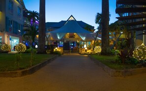 A hotel entrance with a covered walkway, palm trees, and illuminated decorations. - Village Creole (Trois-Ilets)