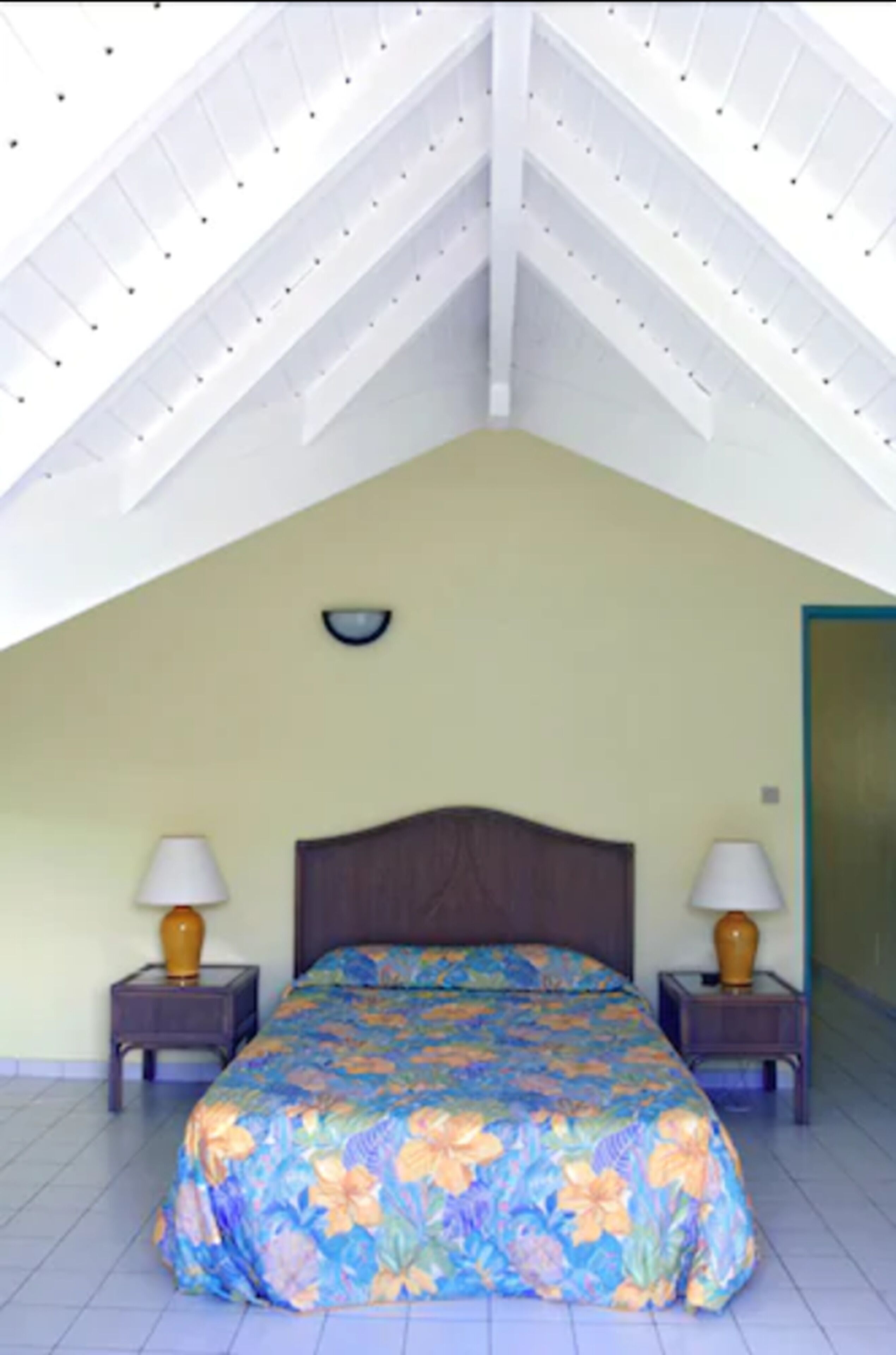 A bedroom with a sloped ceiling, a bed with floral bedding, two bedside lamps, and a nightstand on each side.