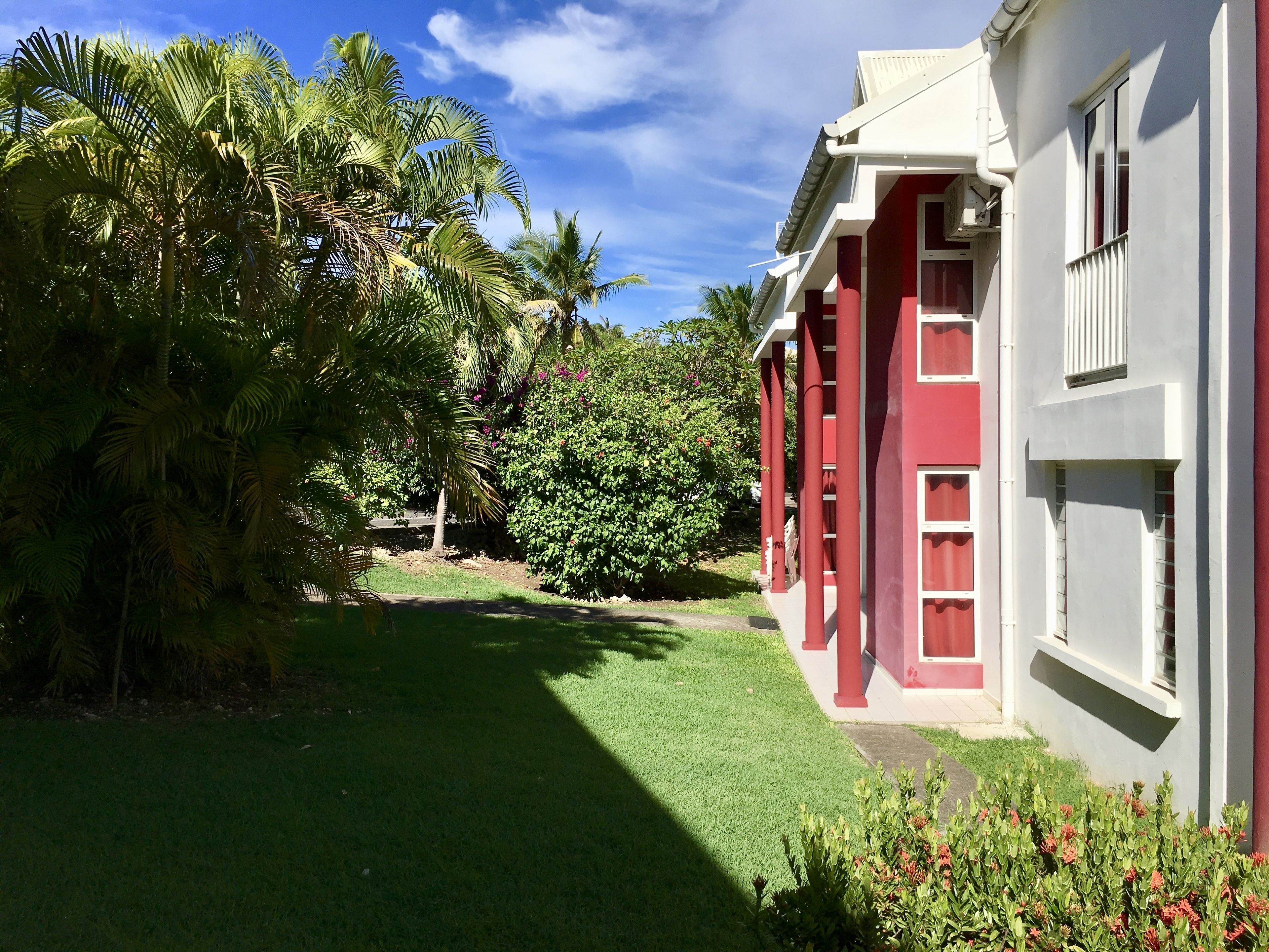 Un edificio con paredes exteriores rojas y blancas, un césped cuidado y palmeras.