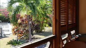 Un porche de madera con vistas a un jardín, que incluye una palmera y plantas coloridas.