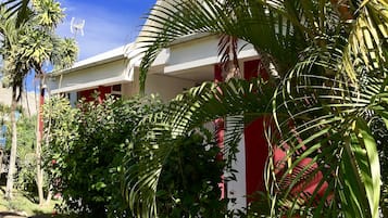 Un bâtiment à la façade rouge et blanche, entouré d’une végétation luxuriante et de palmiers.