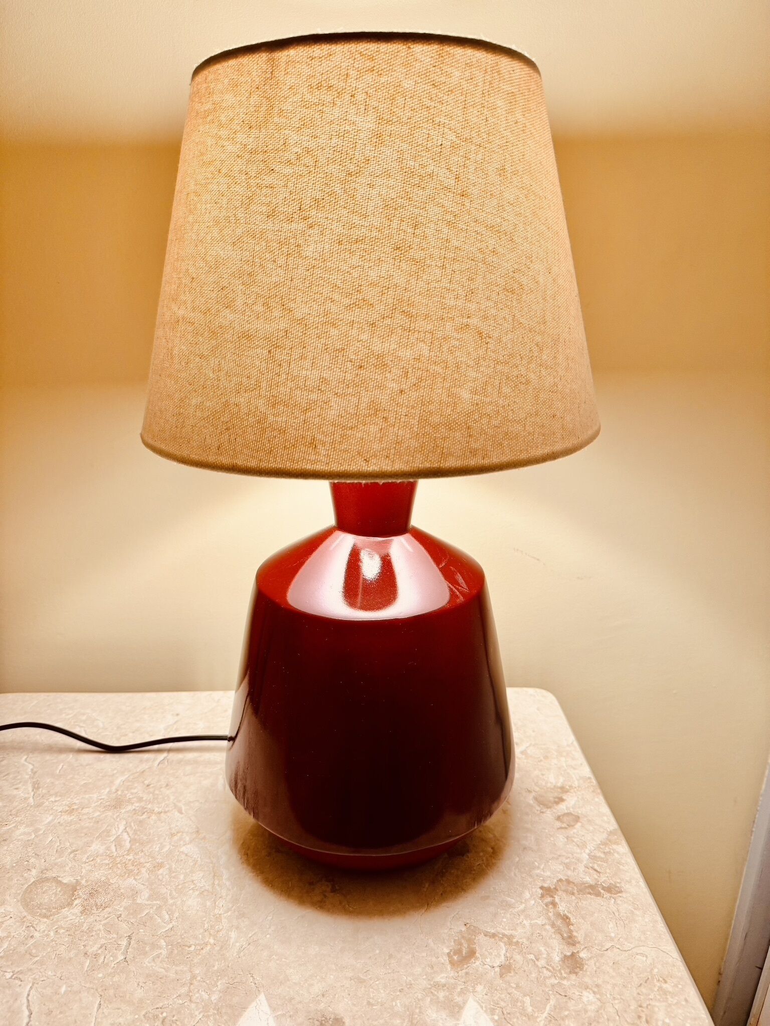 A red table lamp with a beige lampshade on a marble surface.
