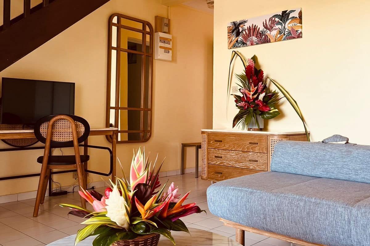 A living room with a sofa, a round table with a plant, a TV, a wooden chair, a staircase, and a wall with artwork.