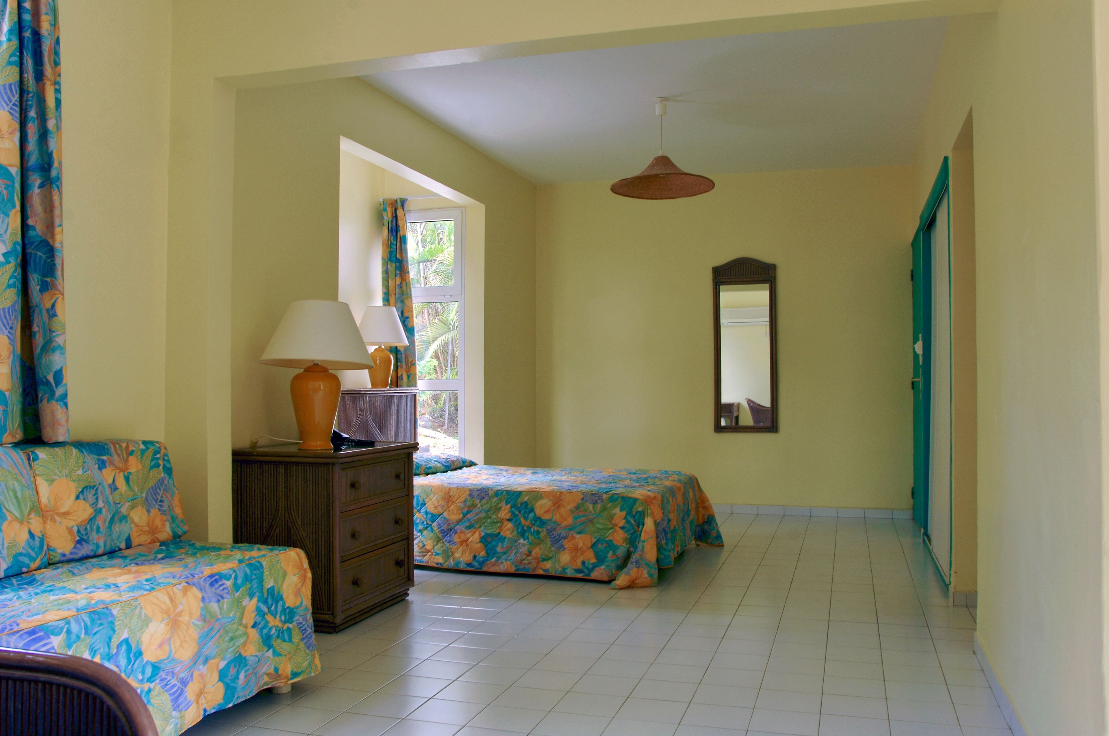 A room with two beds, a dresser, a window with curtains, and a hanging light fixture.