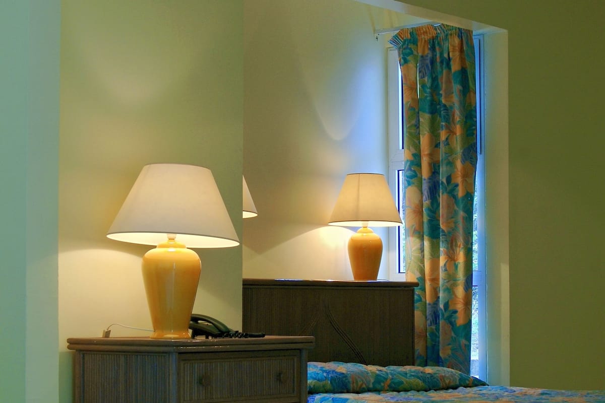 A hotel room with a bed, two lamps, a dresser, and a window with curtains.