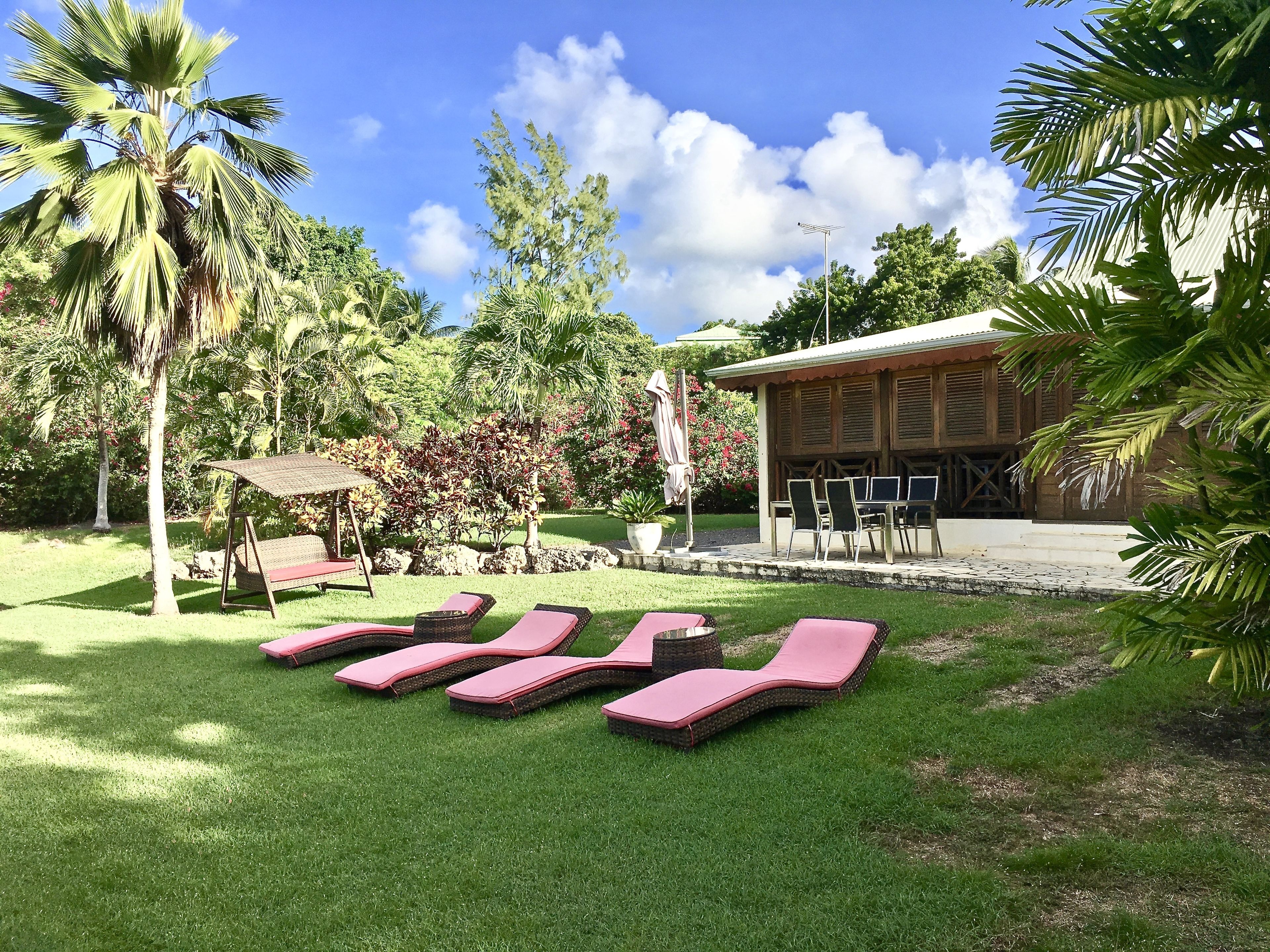 Un jardin avec une piscine, des chaises longues, un bâtiment en bois et des palmiers.