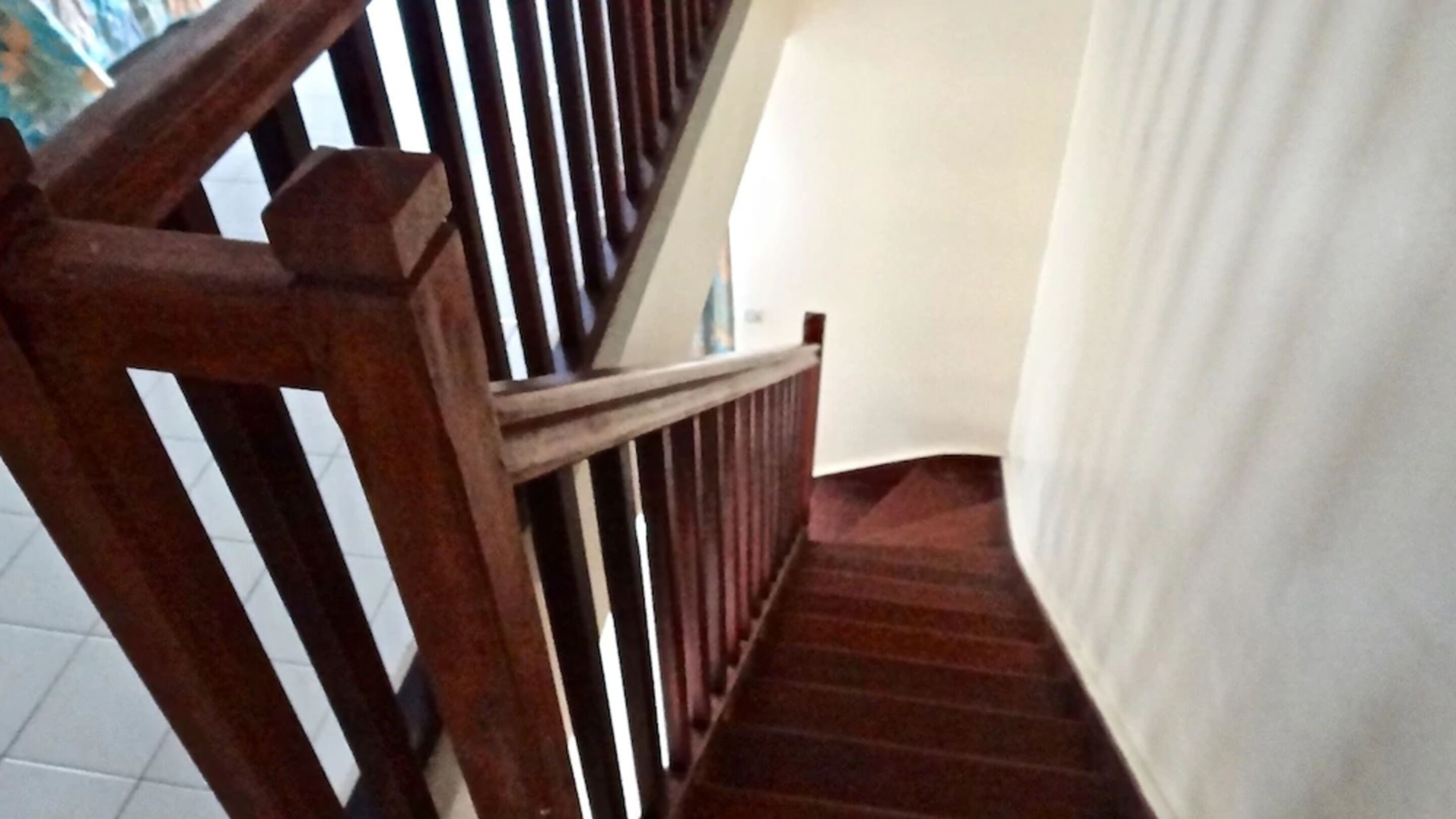 Una escalera de madera con barandilla, que lleva a un rellano con pared blanca y una puerta.