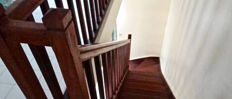 Una escalera de madera con barandilla, que lleva a un rellano con pared blanca y una puerta.