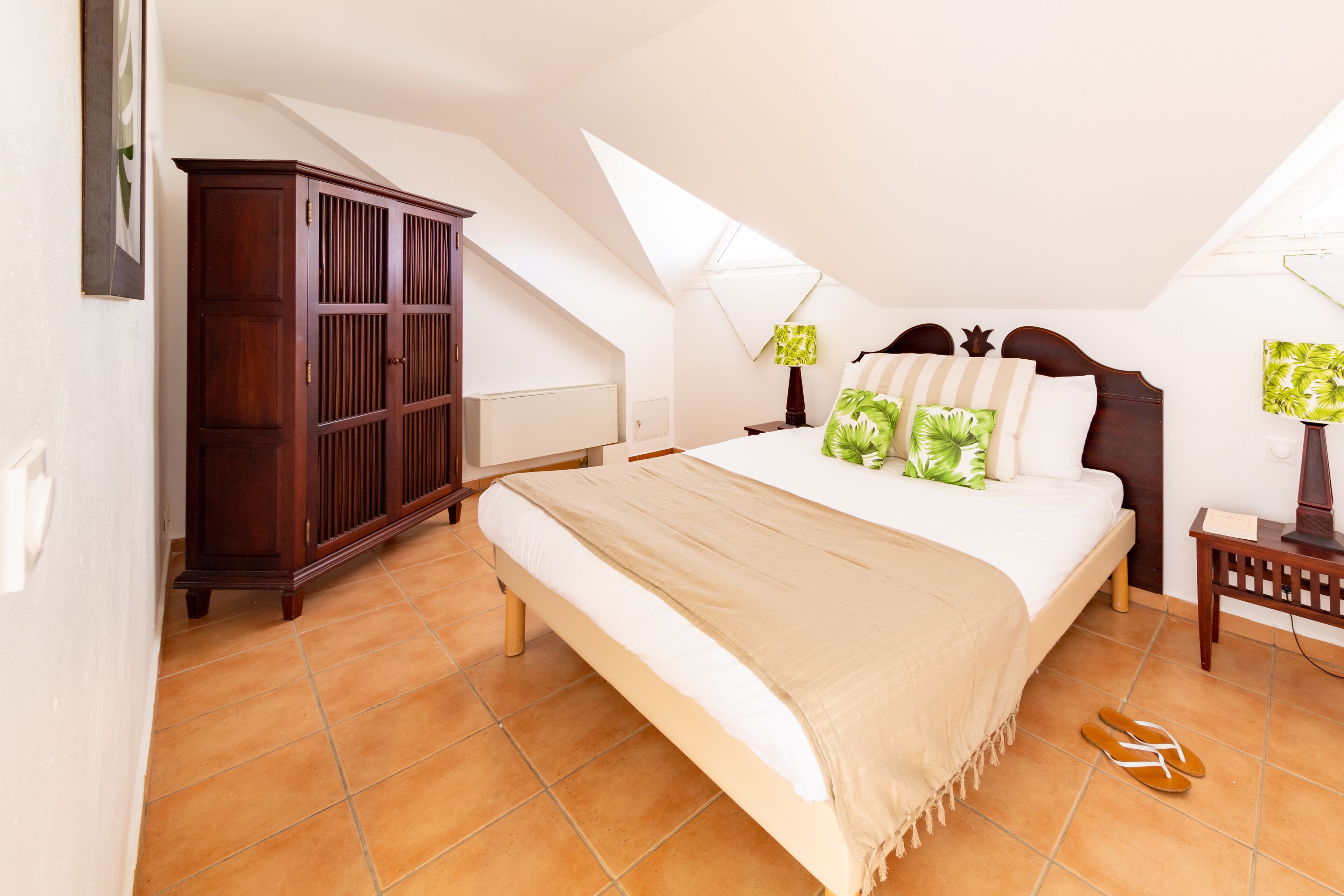 A bedroom with a large bed, a wardrobe, and a nightstand with a lamp.